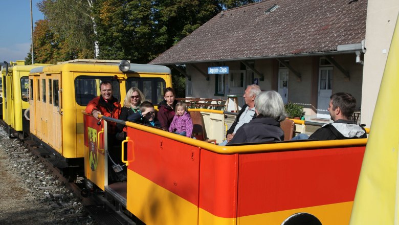 Zayatal rail cab, © VNLB People sit in a yellow and red rail cab in front of a station building.