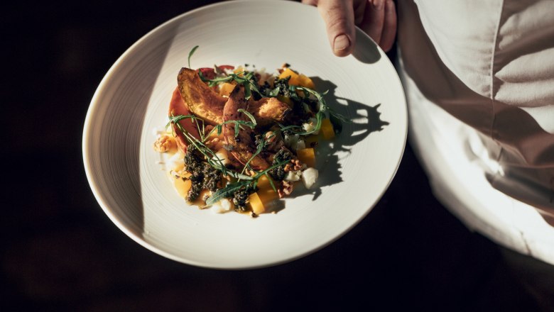 Gerösteter Hokkaido-Kürbis, Salbeipesto, Schafkäse, © Niederösterreich Werbung/Julius Hirtzberger Ein Teller mit geröstetem Hokkaido-Kürbis, Salbeipesto und Schafkäse, gehalten von einer Person in weißer Kleidung.