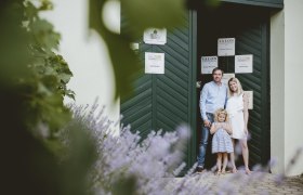 Herzlich Willkommen, © Michael Reidinger Eine Familie steht vor einem grünen Tor, umgeben von Lavendel und Pflanzen.