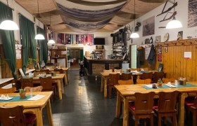 Gaststube, © Andreas Sinnhuber Gemütliche Gaststube mit Holztischen, Stühlen und Bar, dekoriert mit Fußballschals und rustikalen Elementen.