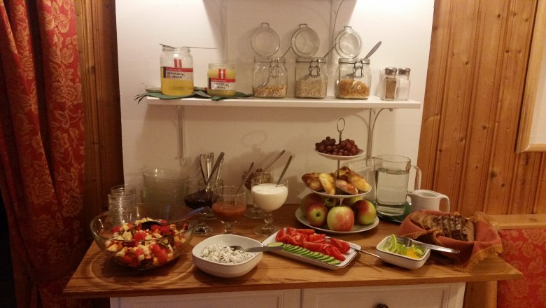 Frühstück, © Familie Fleischmann Ein Frühstücksbuffet mit Obst, Brot, Aufstrichen und Müsli in einem gemütlichen Raum.