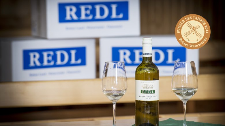 Weingut Redl, © Weingut Redl Weinflasche und Gläser vor Redl-Kartons.