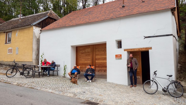 Keller-Wohlfühlplatz beim Kitla Keller, © Initiative Pulkautal / Peter Mödl Menschen sitzen vor einem Kellergebäude mit Fahrrädern.