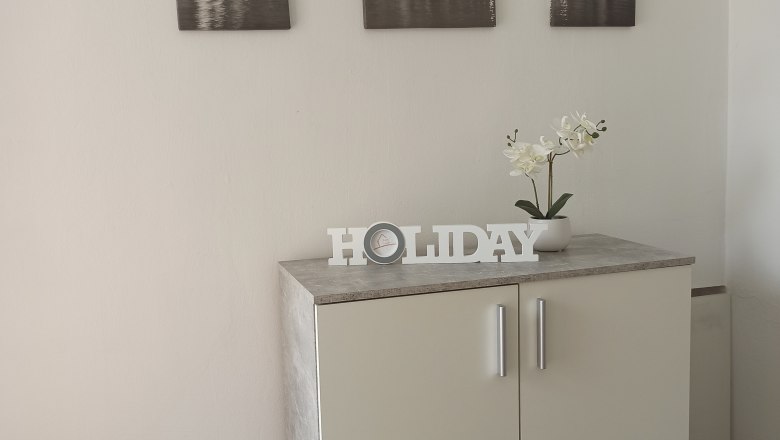 Gemütliches Ambiente, © Multimedia Lauda Ein weißer Schrank mit Dekoration und drei Stadtbildern an der Wand.