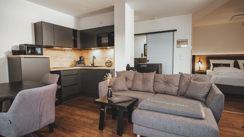 Wohnbereich mit Küchenzeile, © Chalaalets Moderner Wohnbereich mit grauem Sofa, Küchenzeile und Esstisch.