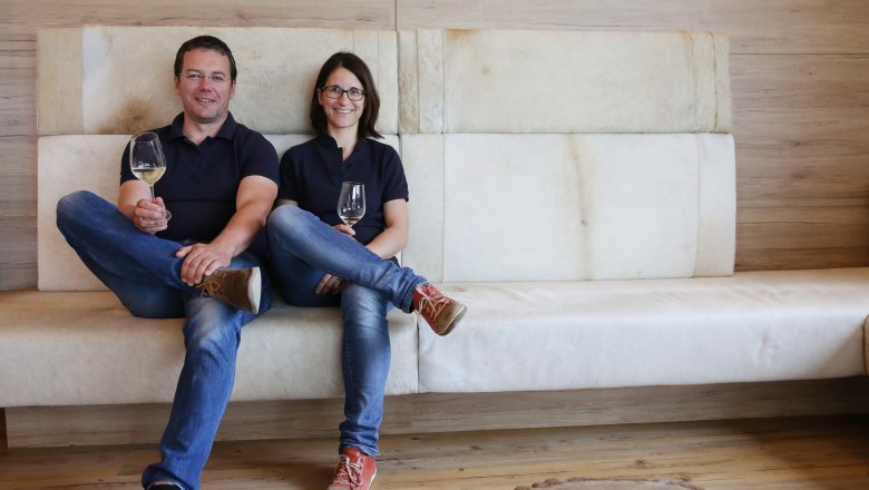 Manfred und Angelika Hebenstreit, © Mathias Karasek Ein Mann und eine Frau sitzen auf einem Sofa und halten Weingläser in der Hand.