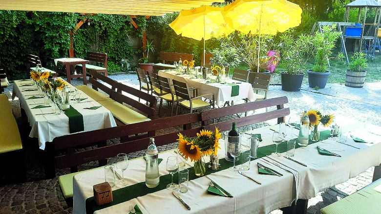 Heurigenlokal Storch, © Schönner Gedeckte Tische im Freien mit Sonnenblumen und gelben Sonnenschirmen.