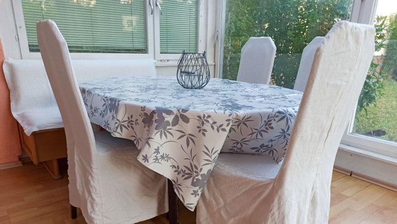 Essbereich, © Multimedia Lauda Essbereich mit Tisch, Stühlen und Bank, Tischdecke mit Blumenmuster, Fenster im Hintergrund.