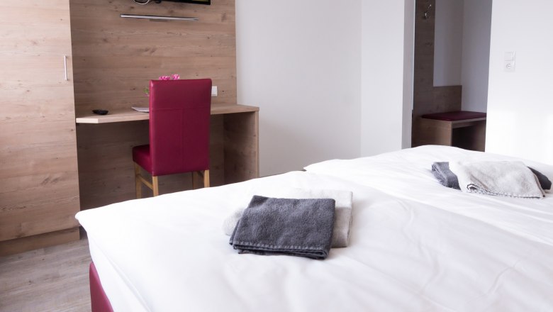 Doppelzimmer, © W. Garhöfer Doppelzimmer mit Bett, Schreibtisch, Stuhl und Fernseher an der Wand.