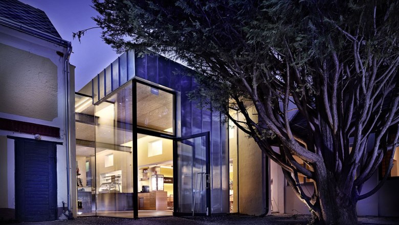 Exterior view, © Andreas Schleissinger Modern glass facade of a building at night, surrounded by trees.
