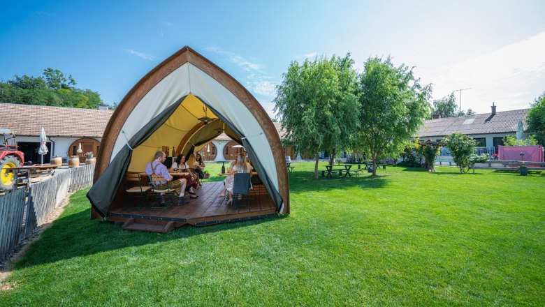 Winery Küssler, © Winzerhof Küssler People sit in an open tent on a meadow, surrounded by trees and buildings.