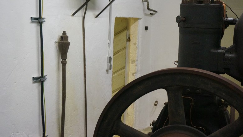 Motor, © K. Vyhnalek Alter Motor in einem Raum mit weißen Wänden und Kabeln.