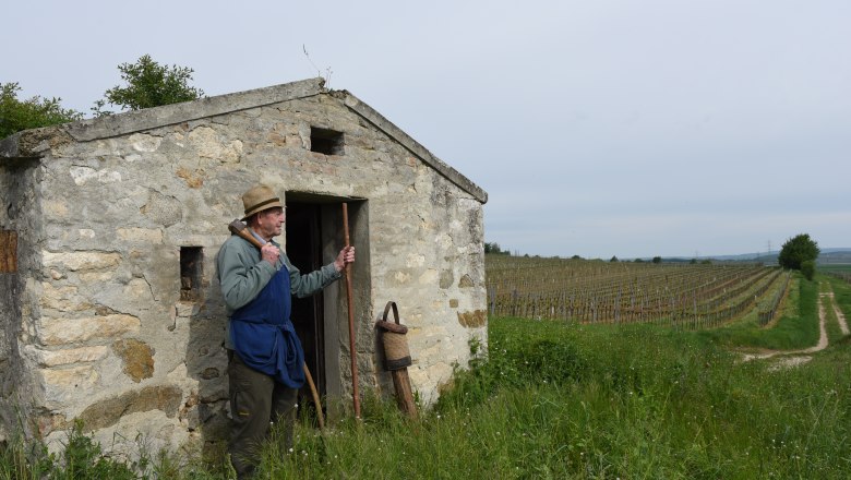 Hiatahittn in Straning, © Harald Veigl Ein Mann mit Strohhut steht vor einer kleinen Steinhütte in einem Weinberg.