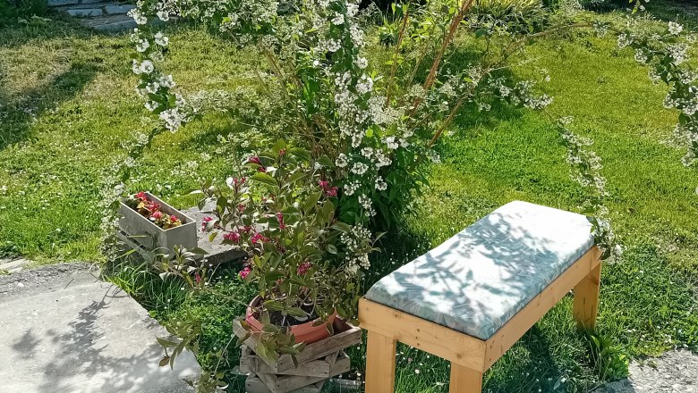 Im Innenhof, © Erna Mitsch Ein grüner Garten mit einer Holzbank, umgeben von blühenden Pflanzen und Blumen.