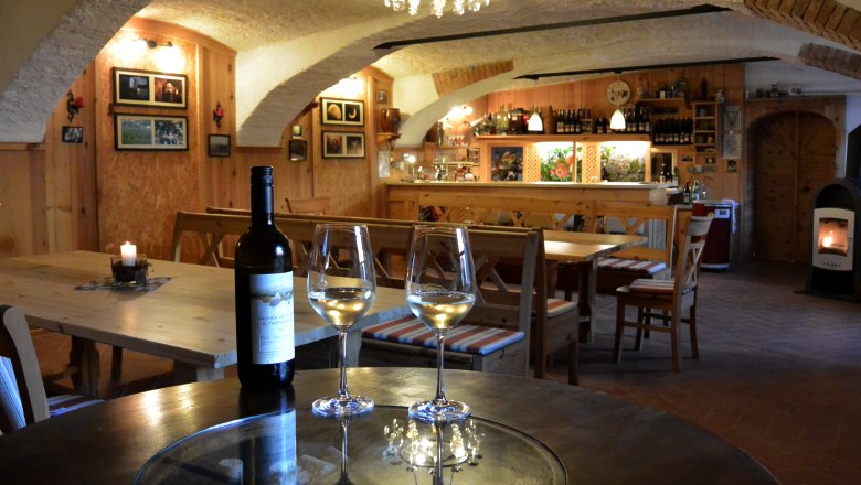 Keller, © Andreas Fischer Gemütlicher Weinkeller mit Holzmöbeln, Weinflasche und Gläsern auf einem Tisch.