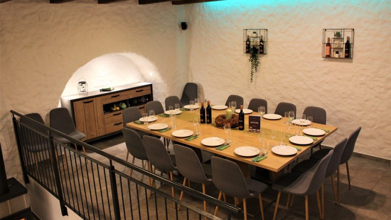 Vinothek, © Weingut Kerner Ein stilvoll gedeckter Tisch in einem Weinkeller mit modernen grauen Stühlen und dekorativer Beleuchtung.