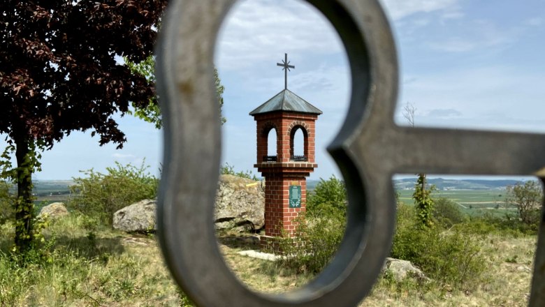 Lord's seat Etzmannsdorf, © Weinstraße Weinviertel A small brick chapel with a cross on a hill, photographed through a heart-shaped metal grid.