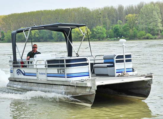 Ferry Wiesbauer Orth/Danube, © Fam. Wiesbauer A small motorboat sails on a river, surrounded by trees on the bank.
