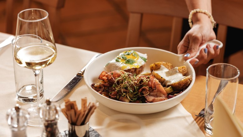 Wein.Restaurant Neustifter, © Weinviertel Tourismus / Michael Reidinger Ein Teller mit Essen und ein Glas Weißwein auf einem gedeckten Tisch.
