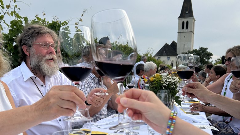 Tafeln im Weinviertel, © Weinviertel Tourismus GmbH Menschen stoßen mit Weingläsern an einem langen Tisch im Freien an, im Hintergrund eine Kirche.