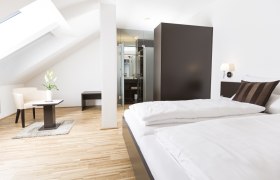 Gästezimmer, © Ernst Jöchlinger Modernes Gästezimmer mit Bett, Sessel und Tisch unter Dachschräge.