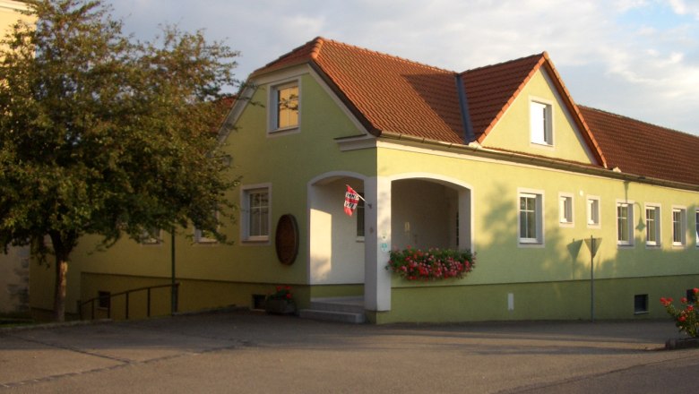 Guest room entrance, © Kurt Englmayer Yellow building with a red roof and flowers at the entrance.