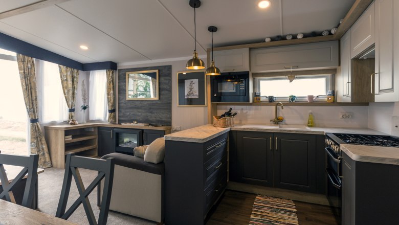 Küche, © Leopold Pluschkowitz Moderne Küche mit dunklen Schränken, Herd, Spüle und Hängelampen.