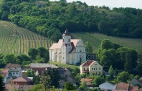 Jakobskirche, © Michael Himml Eine Kirche inmitten von Weinbergen und Häusern, umgeben von grünen Hügeln.