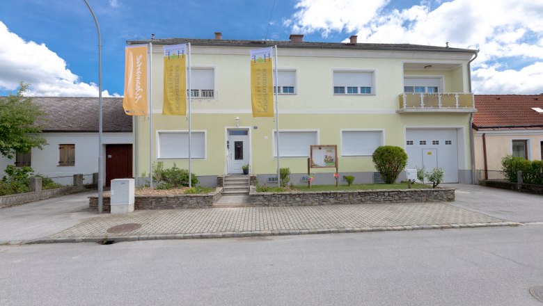 Außenansicht, © Schönfelderhof Außenansicht eines zweistöckigen Gebäudes mit gelber Fassade und zwei Fahnen davor.