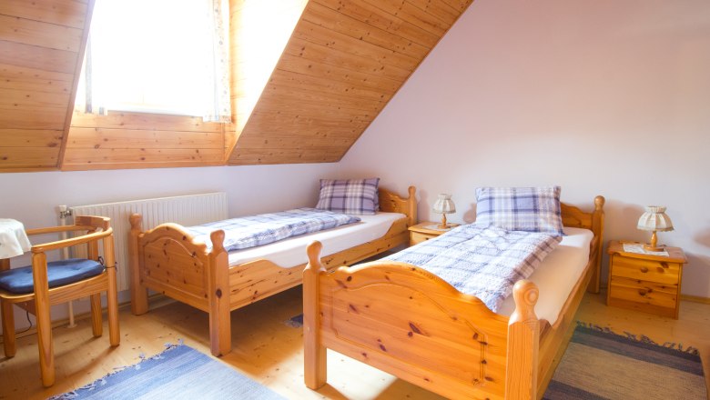 Room with separate beds, © Winzerhof Semmler Cozy bedroom with two single beds made of wood, blue carpets and a window with wooden paneling.