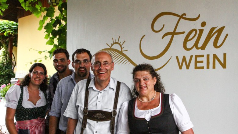 Fein winemaking family, © Familie Fein A group of five people in traditional dress in front of a sign saying 'Fein Wein'.