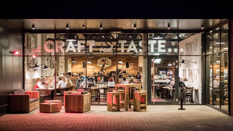 Zündwerk, © Lukas Kirchgasser Photography Außenansicht eines Restaurants mit Glasfront, innen sitzen Menschen an Tischen.