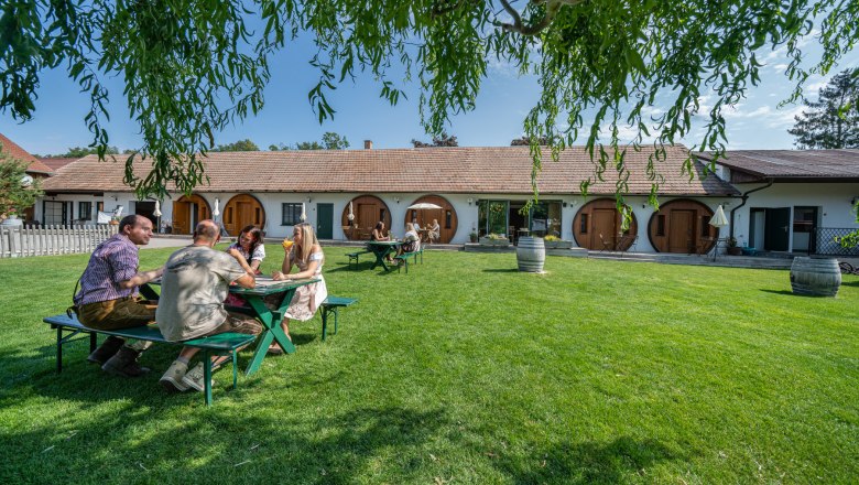 Winery Küssler, © Winzerhof Küssler People are sitting at a table on a lawn in front of a building with round doors.