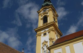 Stadtpfarrkirche Stockerau, © Stadtgemeinde Stockerau Gelber Kirchturm der Stadtpfarrkirche Stockerau vor blauem Himmel.