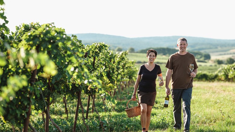 Christina und Robert, © Michael Reidinger Zwei Personen gehen durch einen Weinberg und halten Weingläser in der Hand.