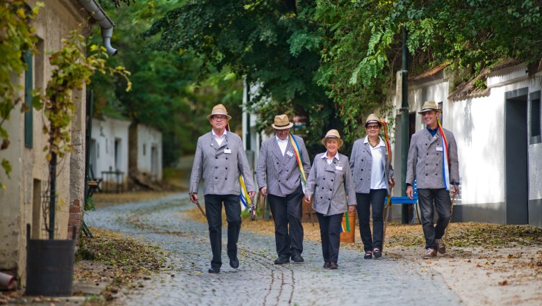 Kellergasse Radyweg, © Vino Versum Poysdorf / Michael Loizenbauer Fünf Personen in traditioneller Kleidung gehen auf einer gepflasterten Straße.