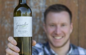 Winzerhof Semmler, © Winzerhof Semmler Ein Mann hält eine Flasche Wein vom Winzerhof Semmler in die Kamera.