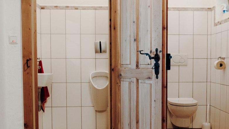 Toiletten, © Weinakademie Retz Zwei Toilettenräume mit Holztür, links ein Urinal und Waschbecken, rechts eine Toilette.