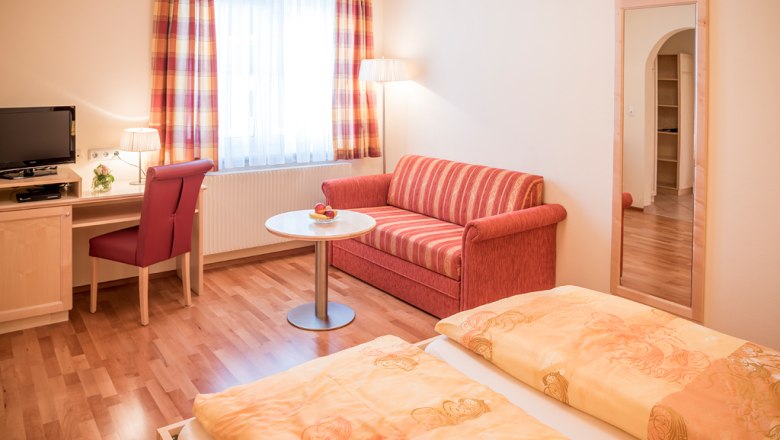 Guest room, © Fam. Breitenfelder Cozy guest room with double bed, red sofa, desk, TV and large mirror.