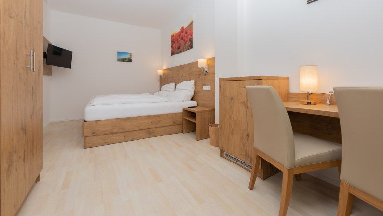 Schlafzimmer, © Schönfelderhof Modernes Schlafzimmer mit Holzmöbeln, Doppelbett, Schreibtisch und Flachbildfernseher.