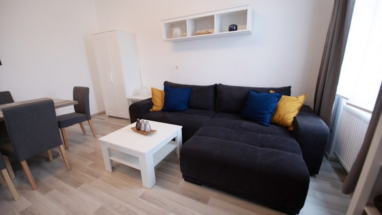 Wohnbereich, © Ferienhaus Scheer Moderner Wohnbereich mit grauem Sofa, bunten Kissen, weißem Couchtisch und Esstisch mit Stühlen.