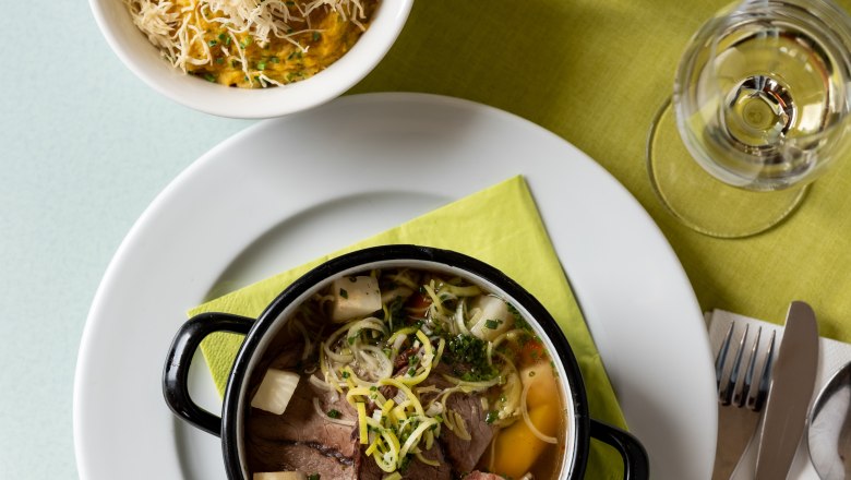 Herbst Inn, © Weinviertel Tourismus / Michael Reidinger A table with a plate of soup, a bowl of porridge with cheese, a glass of water and cutlery on a green napkin.