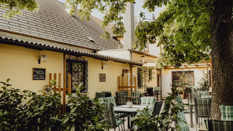 Gasthaus mit Gästehaus in Wulzeshofen, © Niederösterreich Werbung/Sophie Menegaldo Gemütlicher Gastgarten eines Gasthauses mit grünen Stühlen und Tischen unter einem Baum.