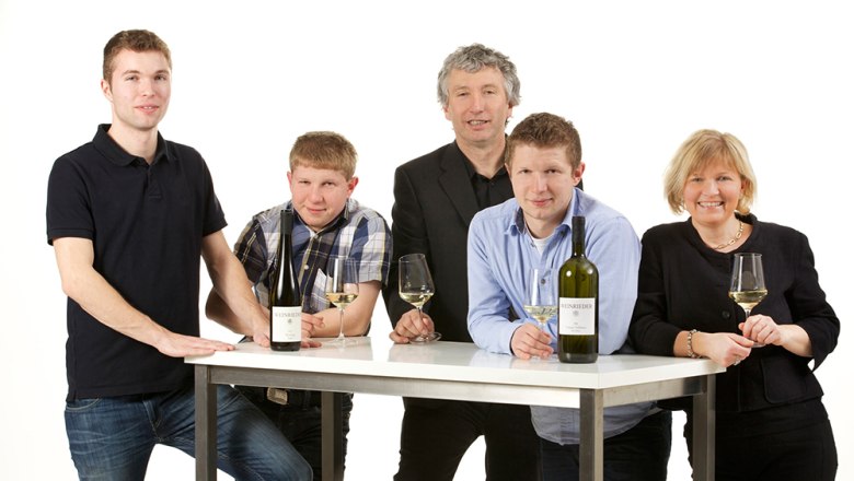 Familie Rieder, © Weinrieder Fünf Personen stehen um einen Tisch mit Weinflaschen und Gläsern.