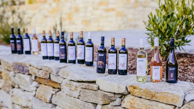 Wine assortment, © Christina Wenzina Row of wine bottles on a stone wall outside.
