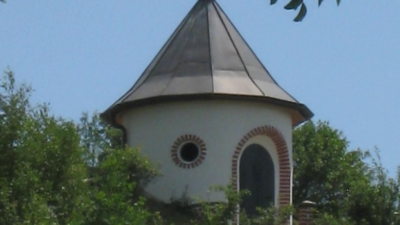 Wasserturm Kammersdorf, © Marktgemeinde Nappersdorf-Kammersdorf Ein runder Wasserturm mit spitzem Dach und Wetterfahne, umgeben von Bäumen und Wiese.