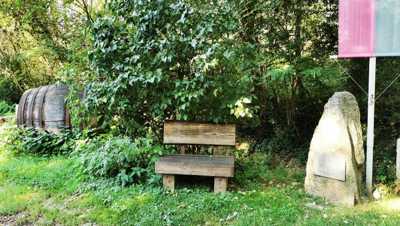 Mozart's pee stone, © Weinstraße Weinviertel Wooden bench next to a stone with an inscription in the greenery.