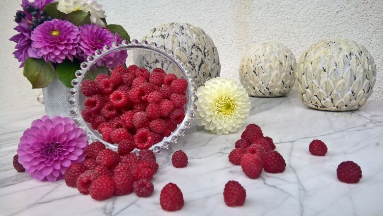 Beerenhof Prenner, © Trixi Rollin Himbeeren in einer Schale mit Blumen und Dekokugeln auf einem Marmortisch.