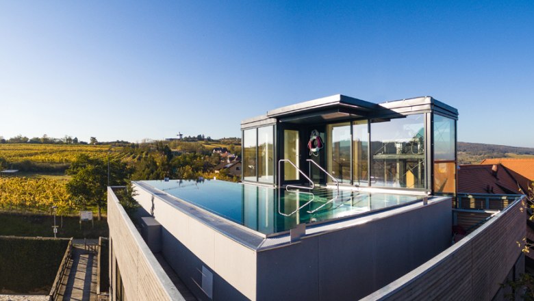 Roof pool, © Althof Retz Rooftop pool with glass walls on a modern building surrounded by countryside.