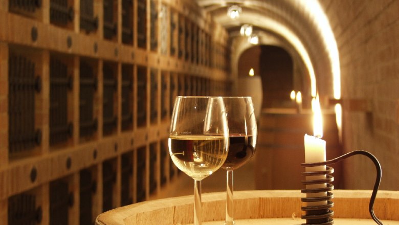 Vinothek, © Burger Zwei Weingläser und eine Kerze auf einem Fass in einem Weinkeller.